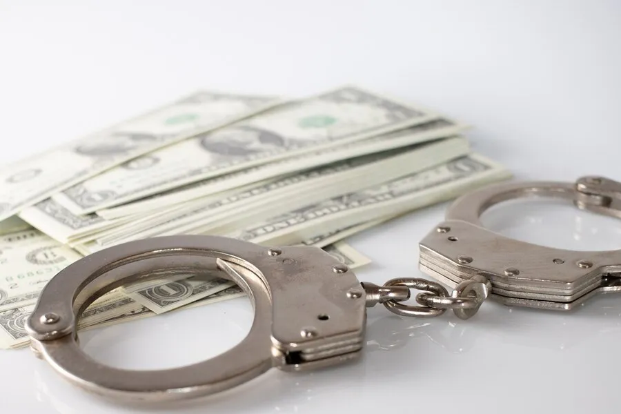 high-angle-shot-metal-handcuffs-some-dollar-bills-white-surface_181624-25411